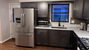 A modern kitchen with stainless steel appliances, dark cabinetry, and a window with blue curtains. - Entire Residential home (Darien)