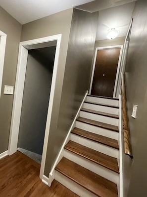 Una escalera de madera con barandillas blancas que conduce a una puerta con una lámpara colgante encima.