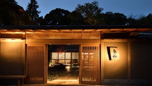 Une entrée de style japonais traditionnel, avec des portes coulissantes et un chemin de pierre menant à un espace aménagé pour s’asseoir.
