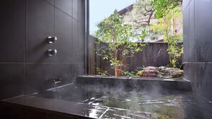 Un spa moderne doté d’un bain à remous, de murs recouverts de carreaux foncés et offrant une vue sur une clôture en bois et des arbres.