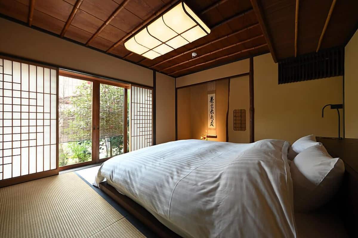 A traditional Japanese-style bedroom with tatami flooring, a large bed, sliding doors, and a ceiling light fixture.