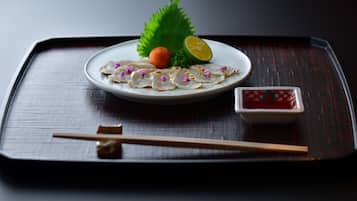 A plate of sashimi with a slice of lemon, a small orange ball, and a decorative leaf on a dark tray.