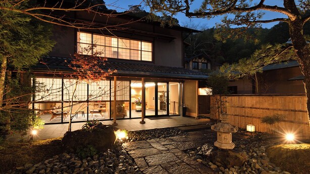 Une maison traditionnelle japonaise, avec un chemin de pierre menant à l’entrée, entourée d  ’une clôture en bambou et d’une lanterne en pierre.