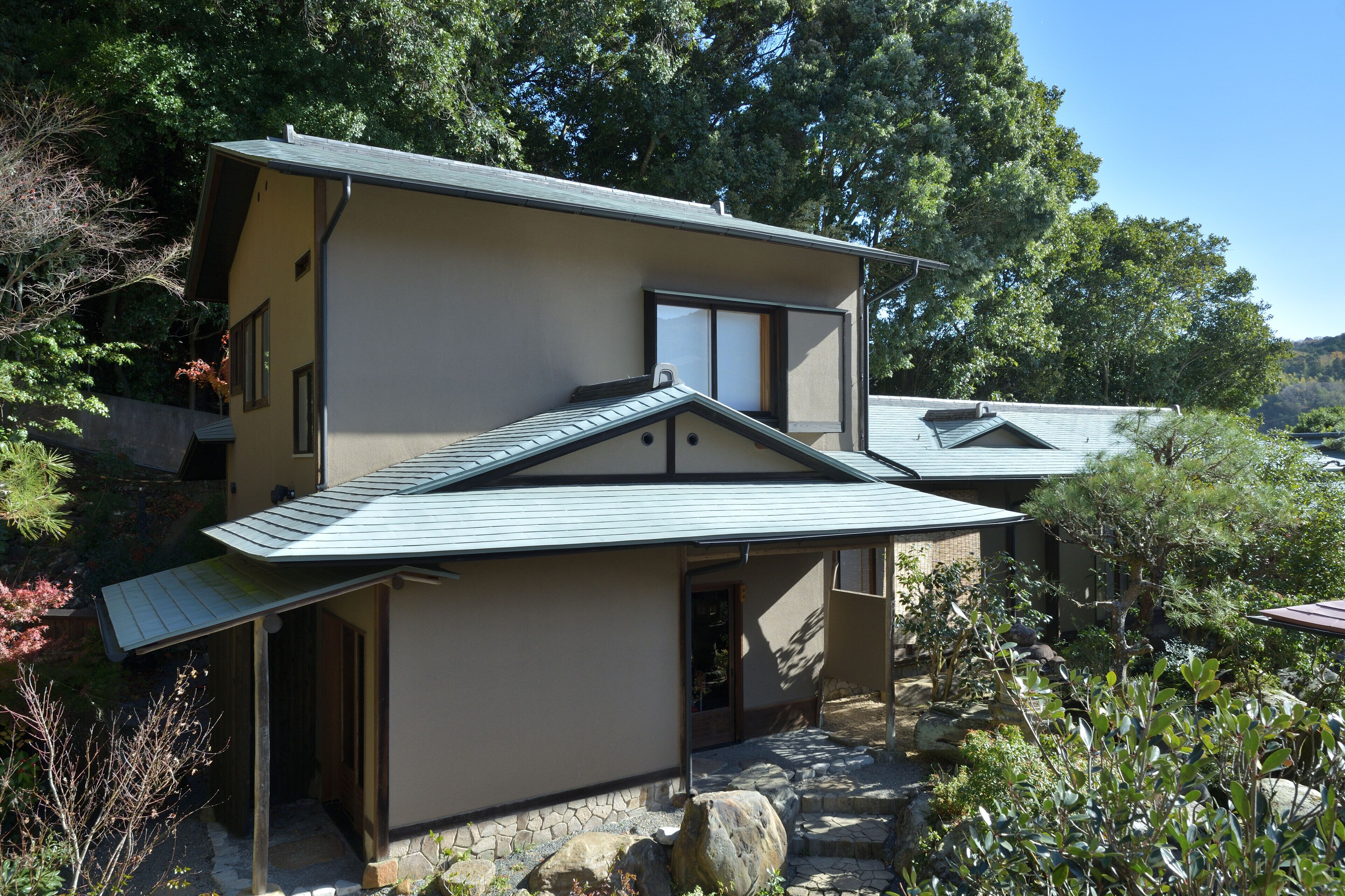 A two-story house with a sloped roof, stone pathway, and surrounding greenery.