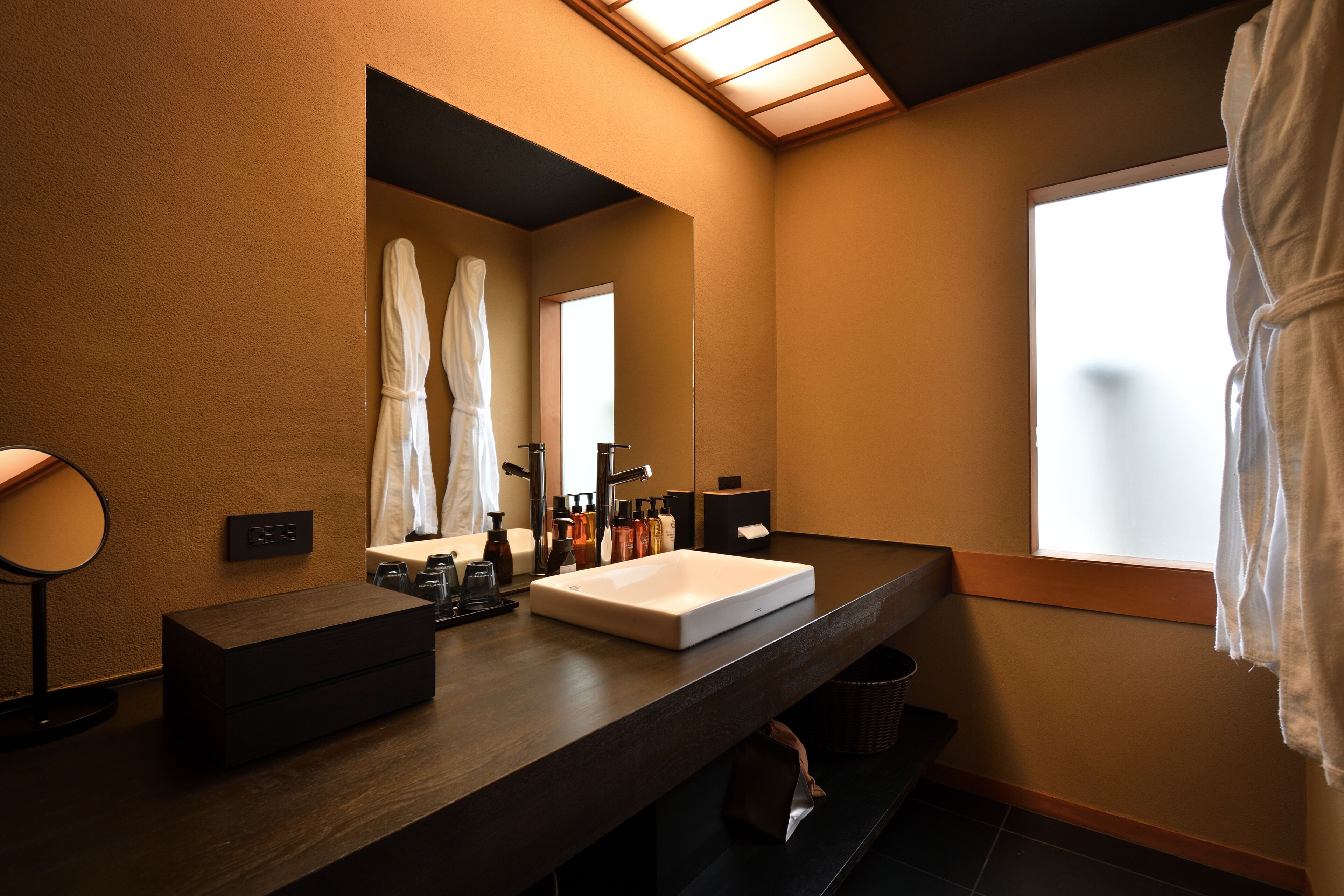 A modern bathroom with a large mirror, a white sink, and a window with a view.