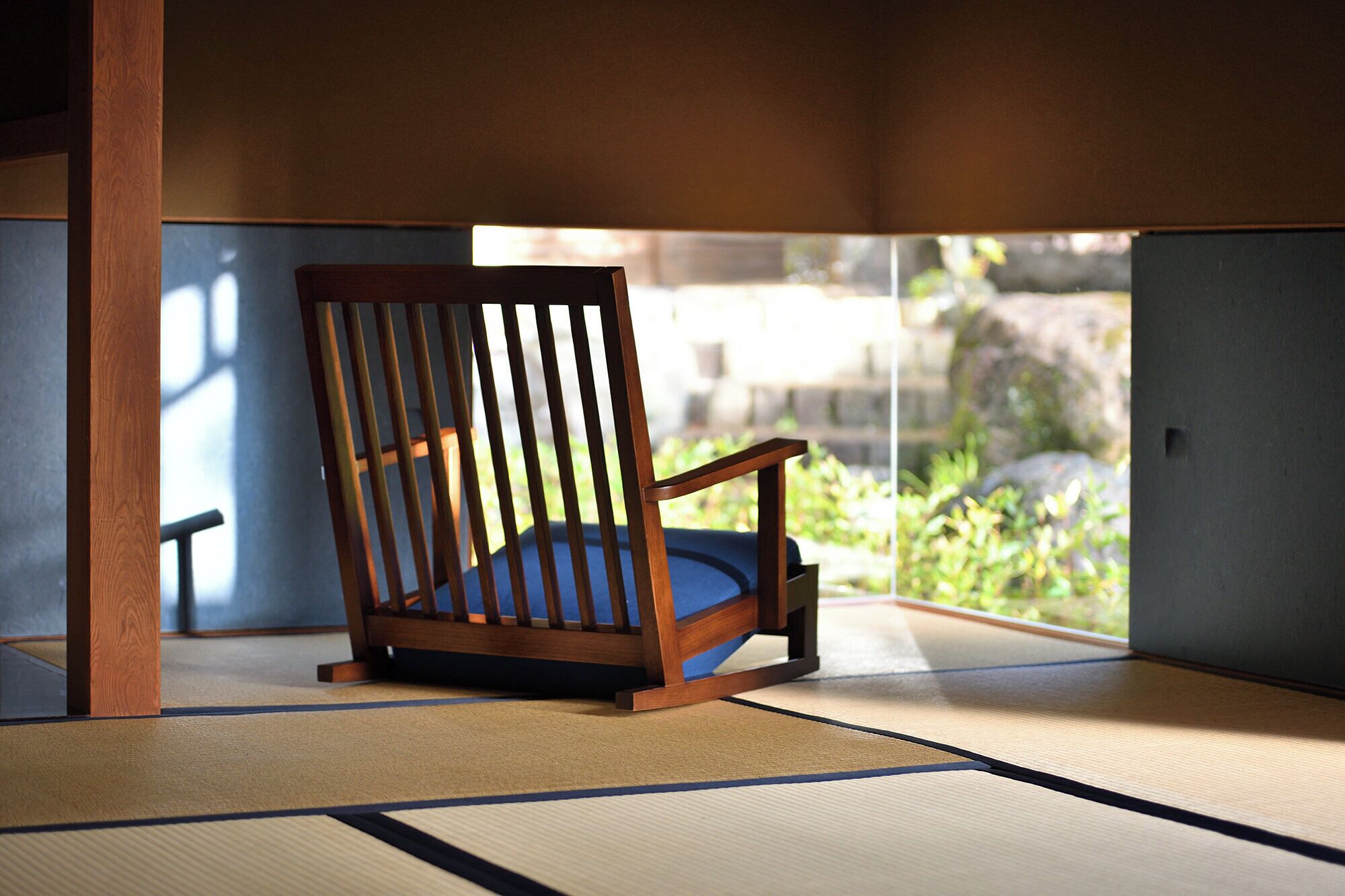 A tatami mat room with a wooden chair and a view of greenery outside.