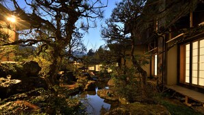 Un jardin japonais traditionnel avec un bassin à carpes koï, des allées en bois et un bâtiment doté de portes coulissantes.