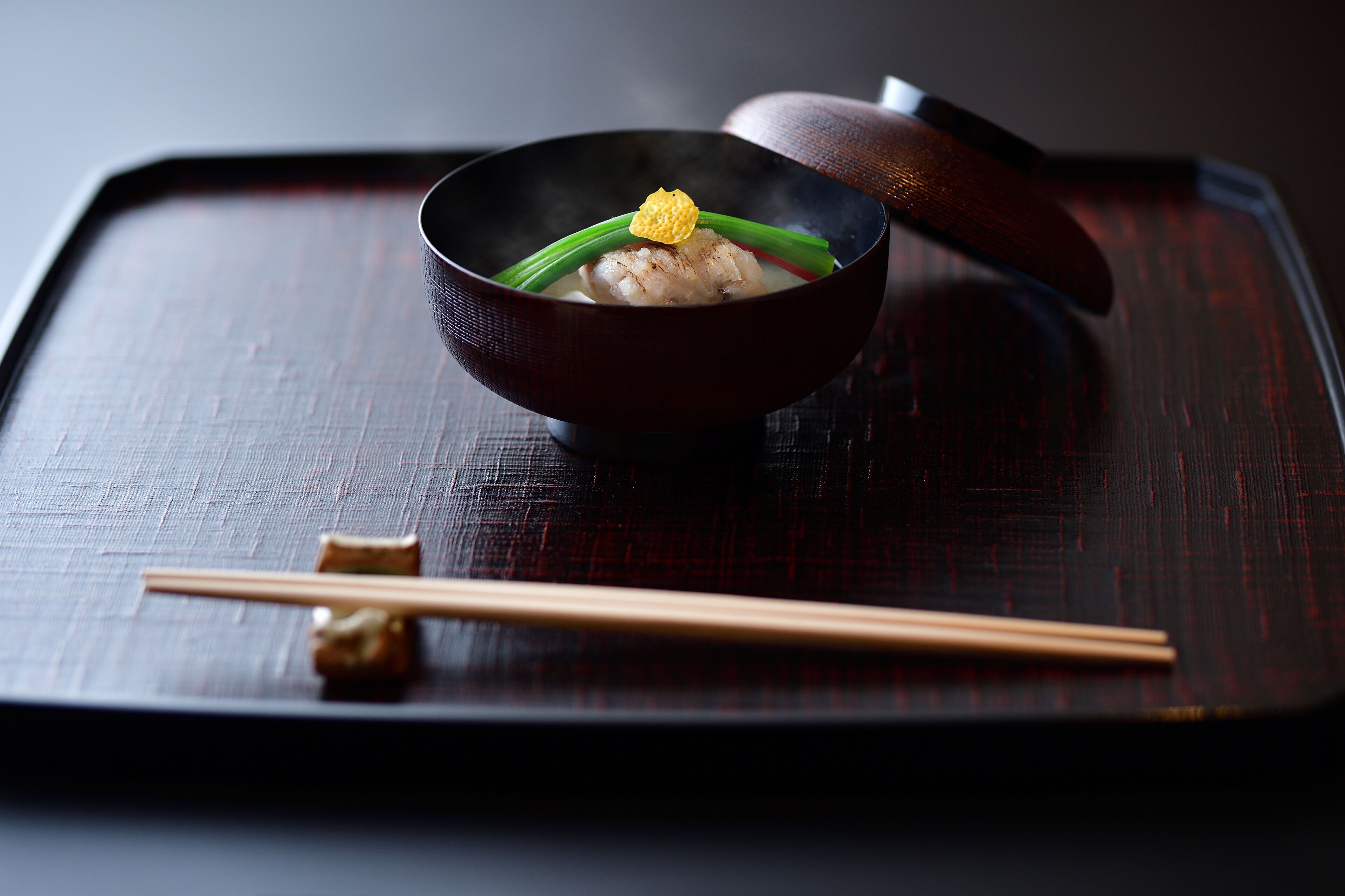 A bowl of food on a dark tray with chopsticks beside it.