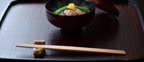 A bowl of food on a dark tray with chopsticks beside it.