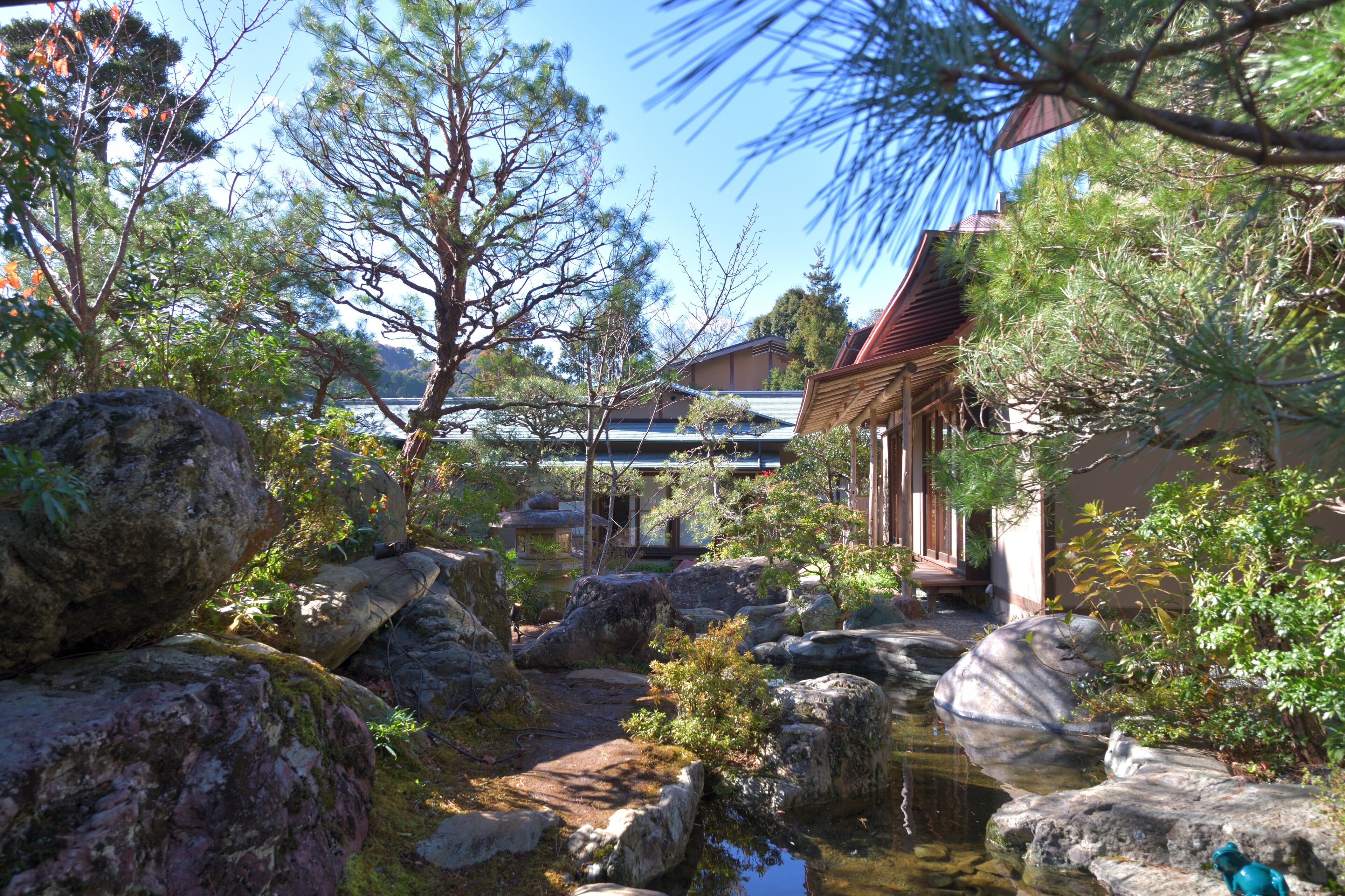 A traditional Japanese garden with a wooden building, large rocks, and a small pond.