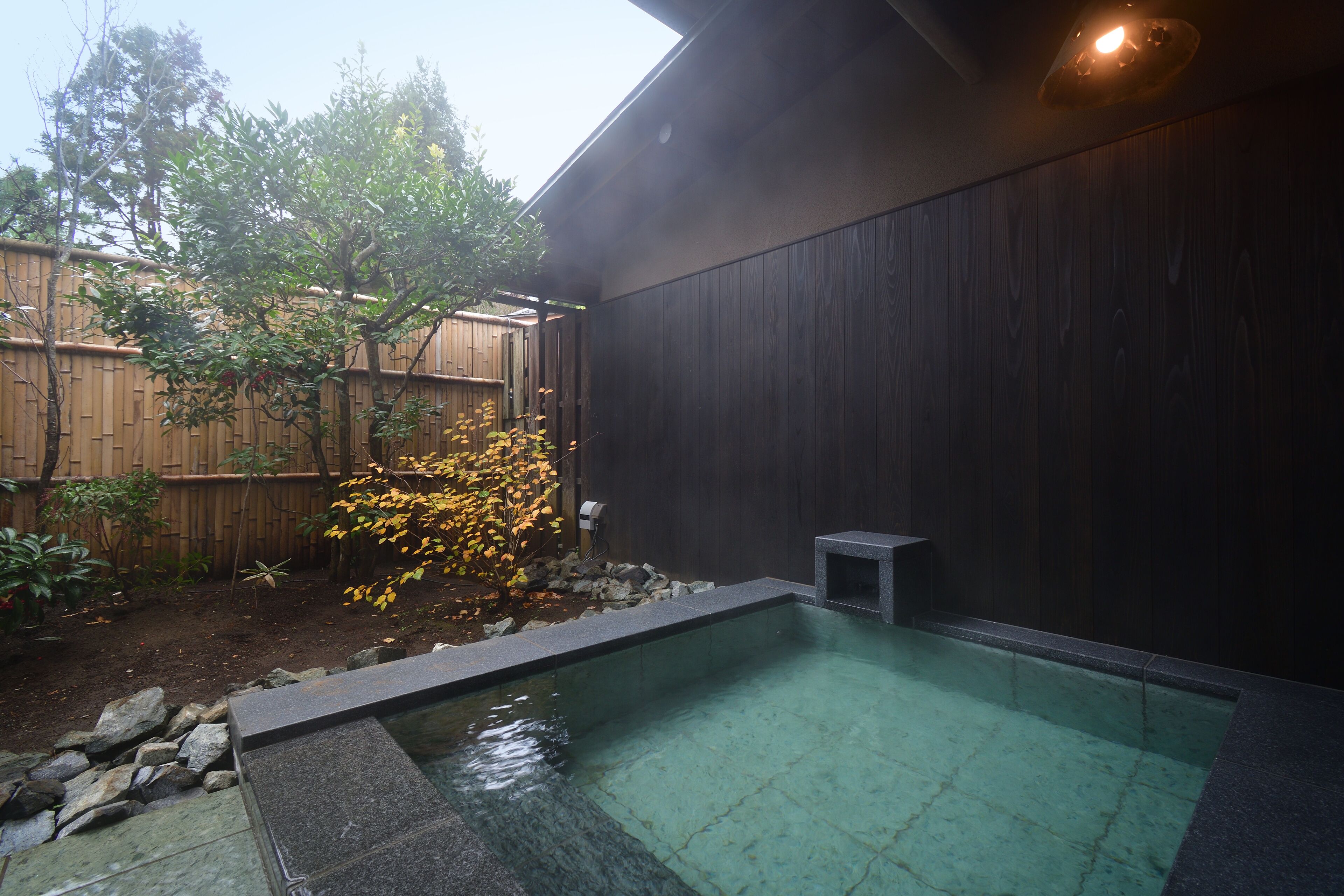A swimming pool with a wooden fence and a small stone structure in a backyard.