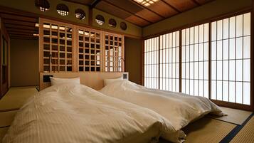 Une pièce de style japonais traditionnel, avec un sol recouvert de tatamis, deux lits avec du linge de lit blanc, un paravent shoji et un plafond en bois.