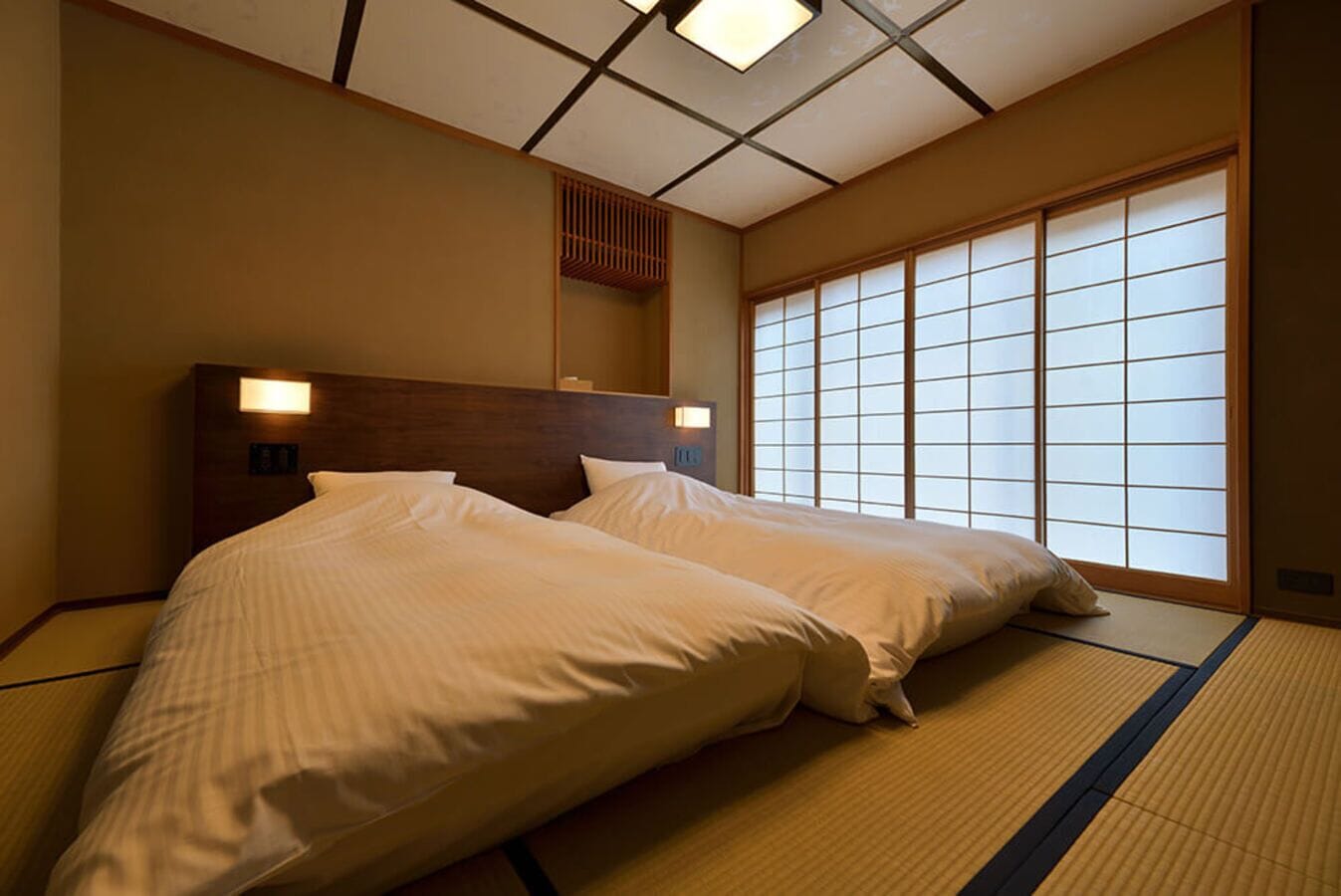 A traditional Japanese-style room with tatami flooring, a low wooden headboard, and sliding shoji doors.