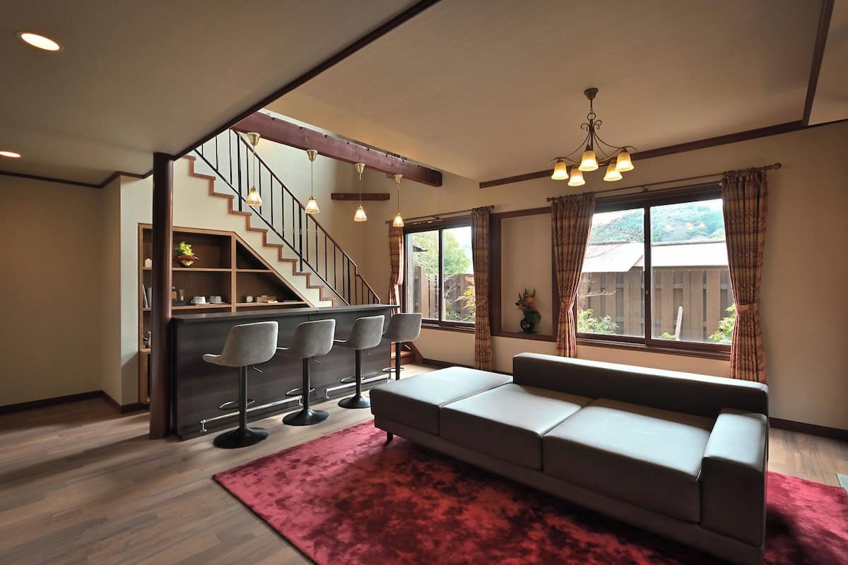 A modern living room with a sofa, a red rug, a staircase, and a bar area with stools.