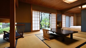 Une pièce de style japonais traditionnel, avec un sol recouvert de tatamis, une table basse, un fauteuil rembourré et des portes coulissantes.