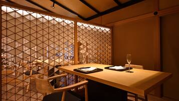 A dining area with a wooden table and chairs, a partition with a geometric pattern, and a view through the partition.