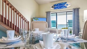 A dining area with a table set for two, a wooden staircase, and a view of the outdoors through a large window. - Gulf Front PCB Condo, Stunning Views, Pool, Balcony, Sleeps 6 (Panama City Beach)