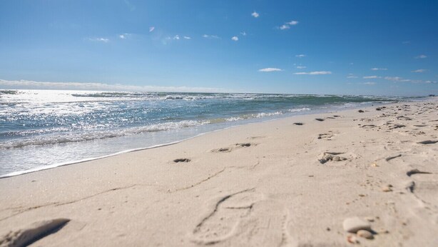 A beach with footprints leading to the water, a clear sky, and a calm sea. - Gulf Front PCB Condo, Stunning Views, Pool, Balcony, Sleeps 6 (Panama City Beach)