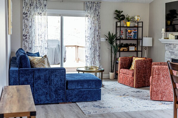 A living room with a blue sofa, red armchairs, a small round table, and a bookshelf.