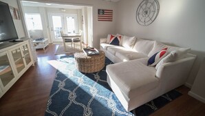Ein Wohnzimmer mit einem weißen Sofa, einem Fernseher und einem Essbereich mit Tisch und Stühlen.