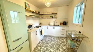 A compact kitchen with white cabinets, a vintage refrigerator, a patterned floor, and a small window.