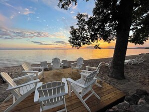 Un pontile in legno con poltrone Adirondack bianche rivolte verso una spiaggia al tramonto.