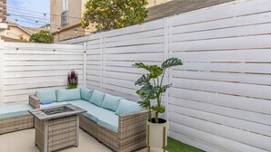 Eine Terrasse mit einem Korbsessel, einem kleinen Tisch und einem Blumentopf.