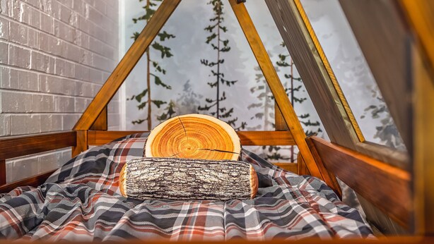 Una estructura triangular de madera acogedora, con una manta escocesa y dos troncos.