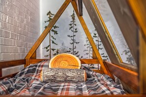 A cozy, triangular wooden tent-like structure with a plaid blanket and two wooden logs. - Family friendly Camp themed condo on Lake Como, minutes to downtown Lake Geneva (Lake Geneva)