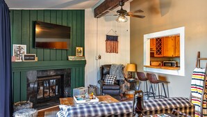 Un salón acogedor con chimenea, un televisor montado en la pared, un sillón cómodo y una mesita con adornos.