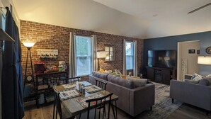 A living room with a sofa, a dining table with chairs, a coffee machine, and a TV.