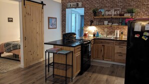 A kitchen with a brick wall, wooden cabinets, a black refrigerator, and a sliding door.