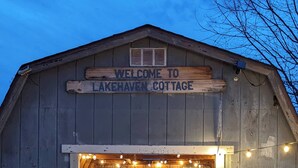 A wooden barn with a sign reading "Welcome to Lakehaven Cottage." Inside, there is a dining area with a table and chairs.