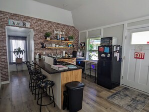 A kitchen with a brick wall, wooden counter, stools, a refrigerator, and a window with blinds. - Relaxing 2 bedroom cottage w/ hot tub and air hockey/ping pong table (Buckeye Lake)