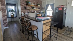 A kitchen with a brick wall, wooden bar stools, a black refrigerator, and a window with curtains.