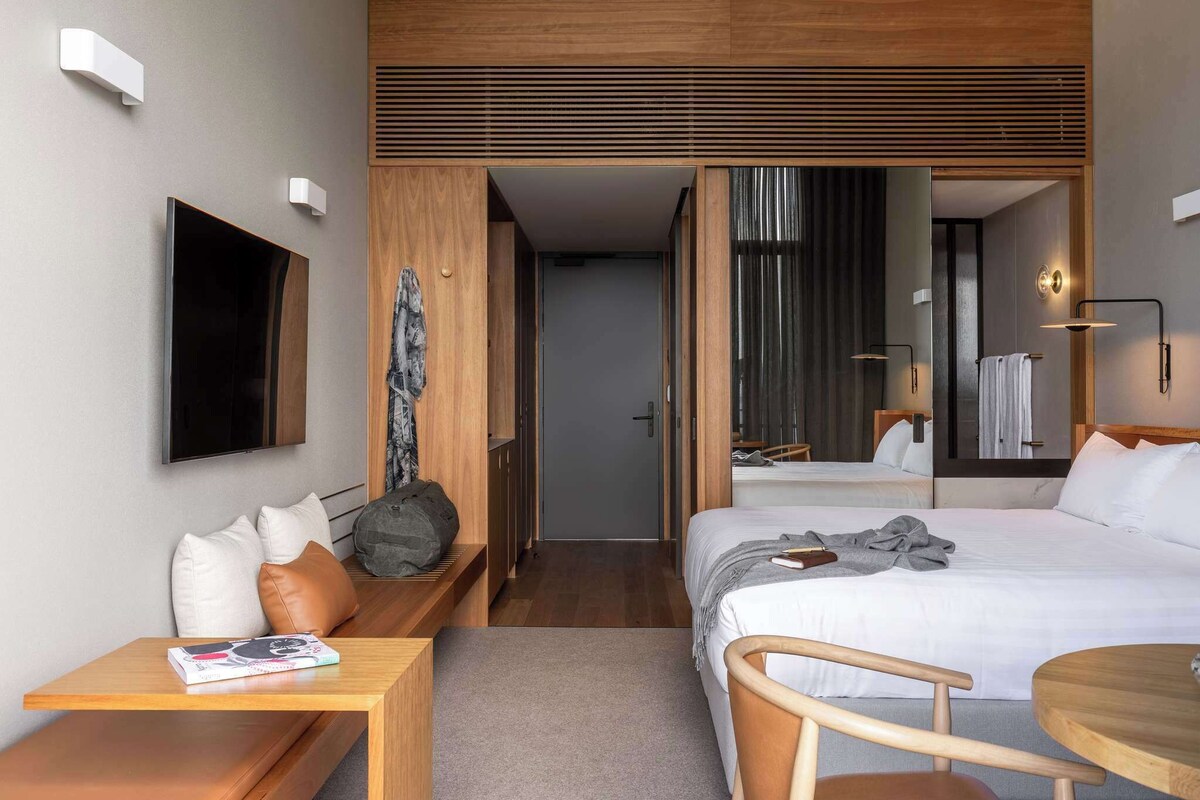 Ein modernes Hotelzimmer mit Bett, Nachttisch, Sessel und einem an der Wand befestigten Fernseher.