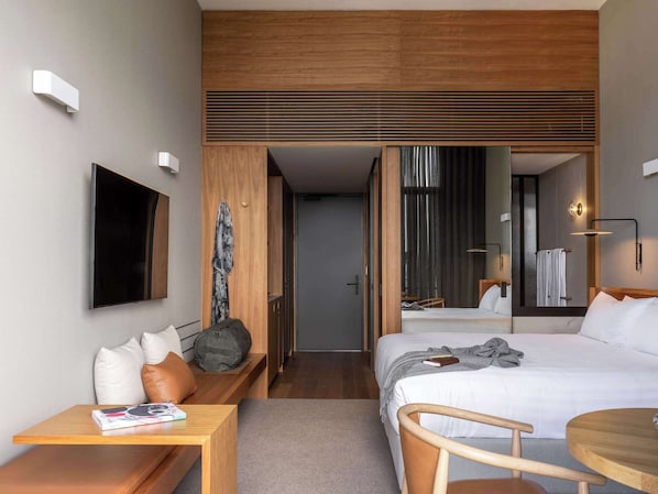 Ein modernes Hotelzimmer mit Bett, Nachttisch, Sessel und einem an der Wand befestigten Fernseher.