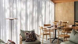 A modern dining area with wooden furniture and a large window with sheer curtains. - Wonil Hotel Perth - Handwritten Collection (Crawley)