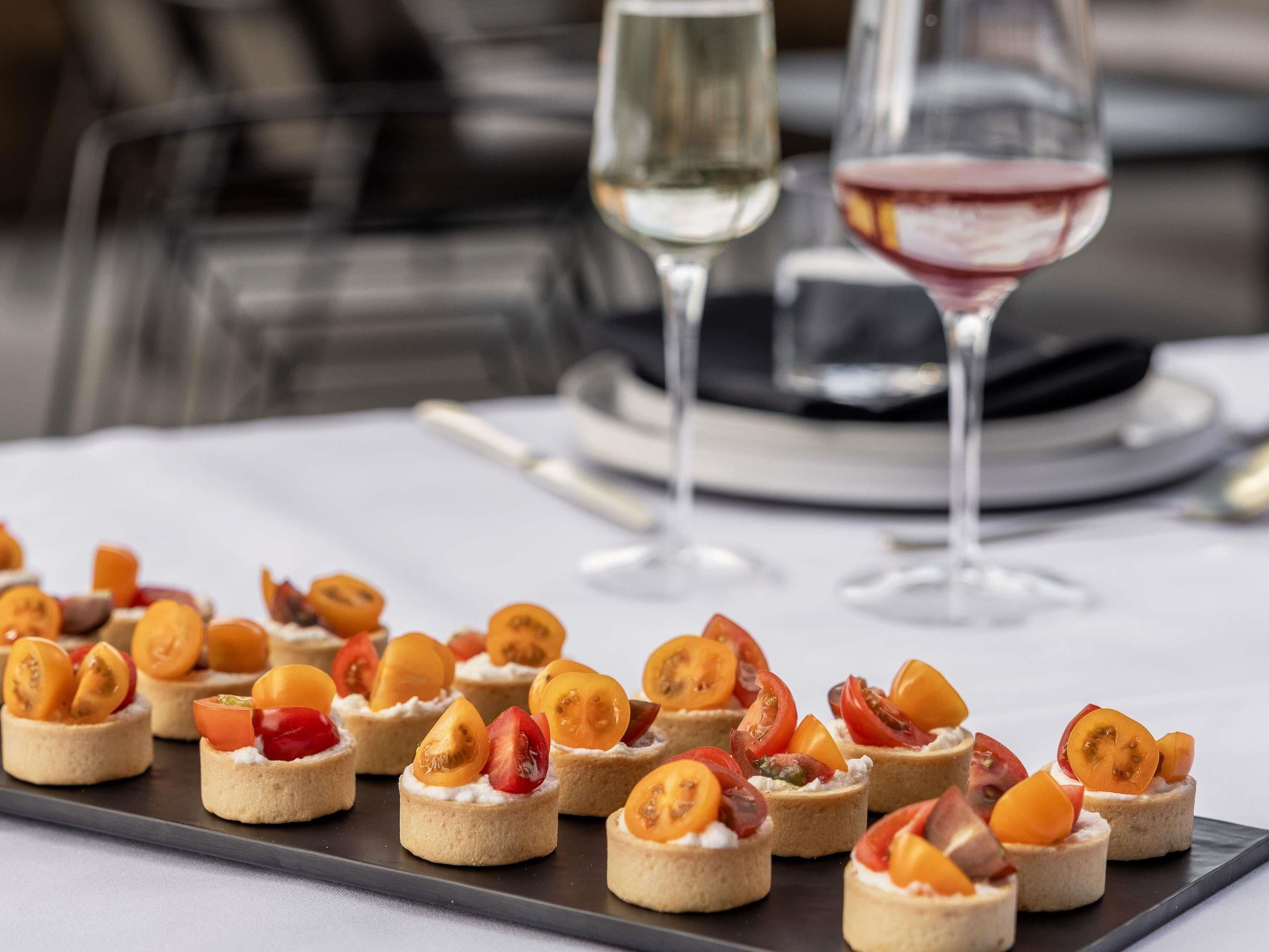 A tray of mini tartlets with fruit toppings, two glasses of wine, and a white tablecloth.