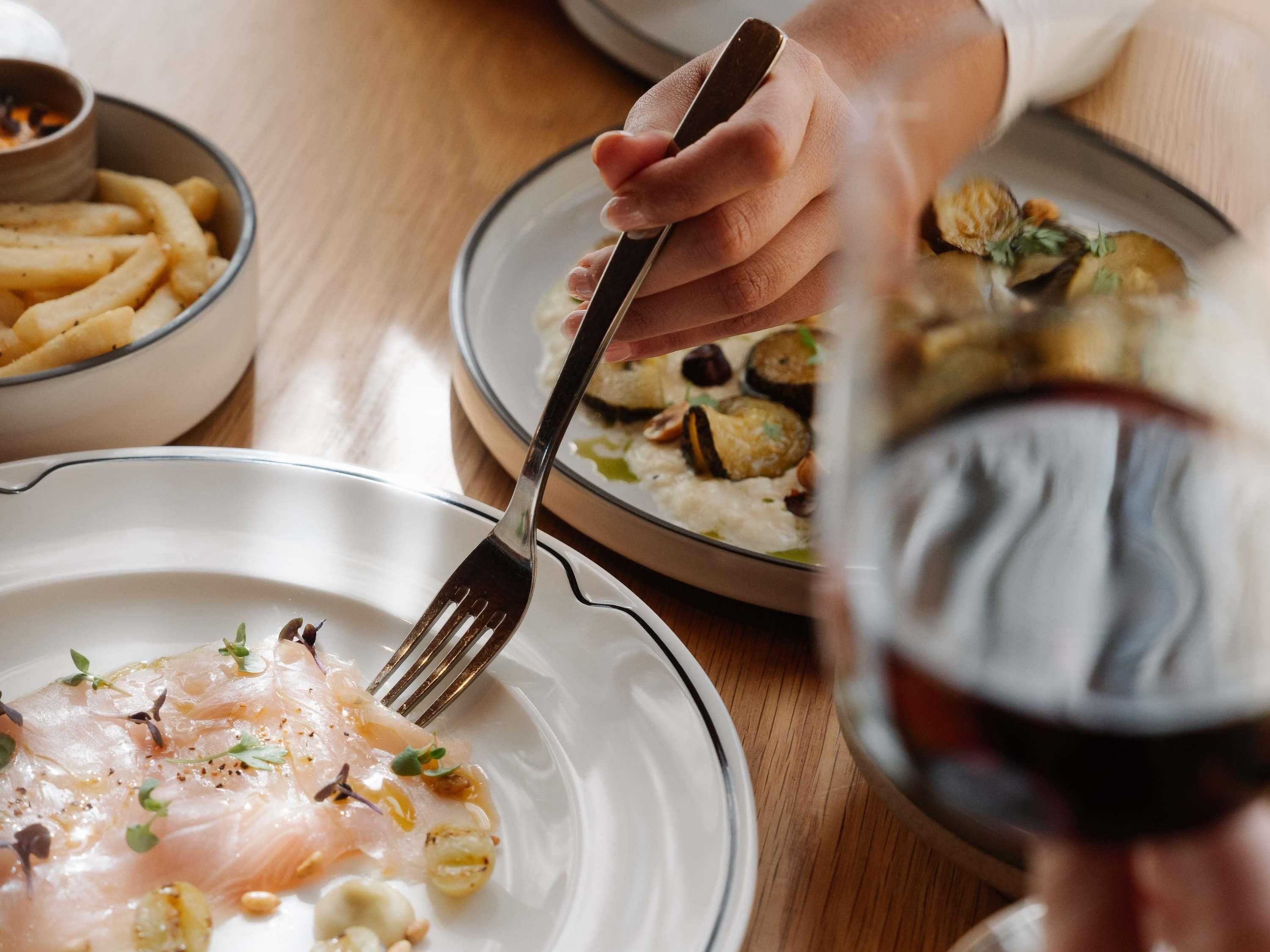 A dining table with plates of food, a fork, and a glass of red wine.