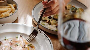 A dining table with plates of food, a fork, and a glass of red wine.