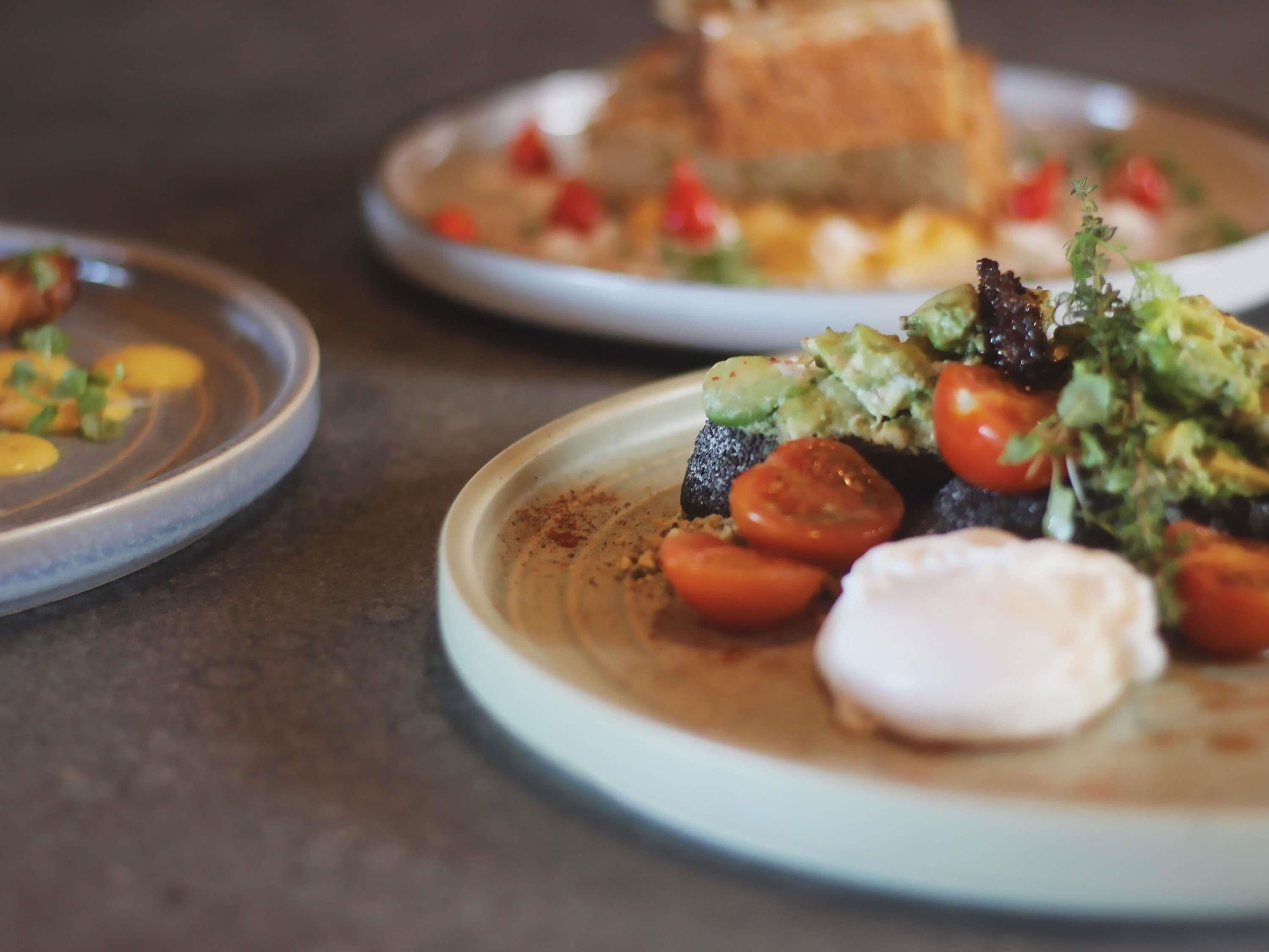 Un plato con ensalada de aguacate y tomate, una rebanada de pan y un recipiente pequeño con una sustancia cremosa.
