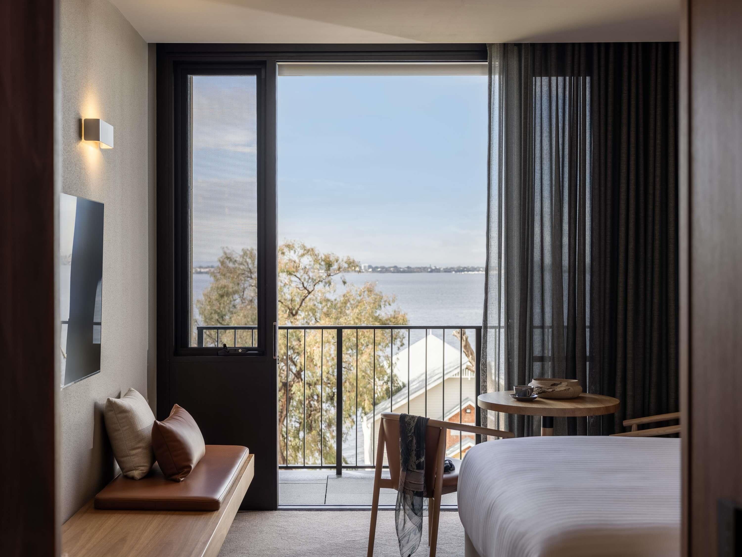Quarto de hotel com uma janela grande, cama, área de estar e uma pequena mesa.