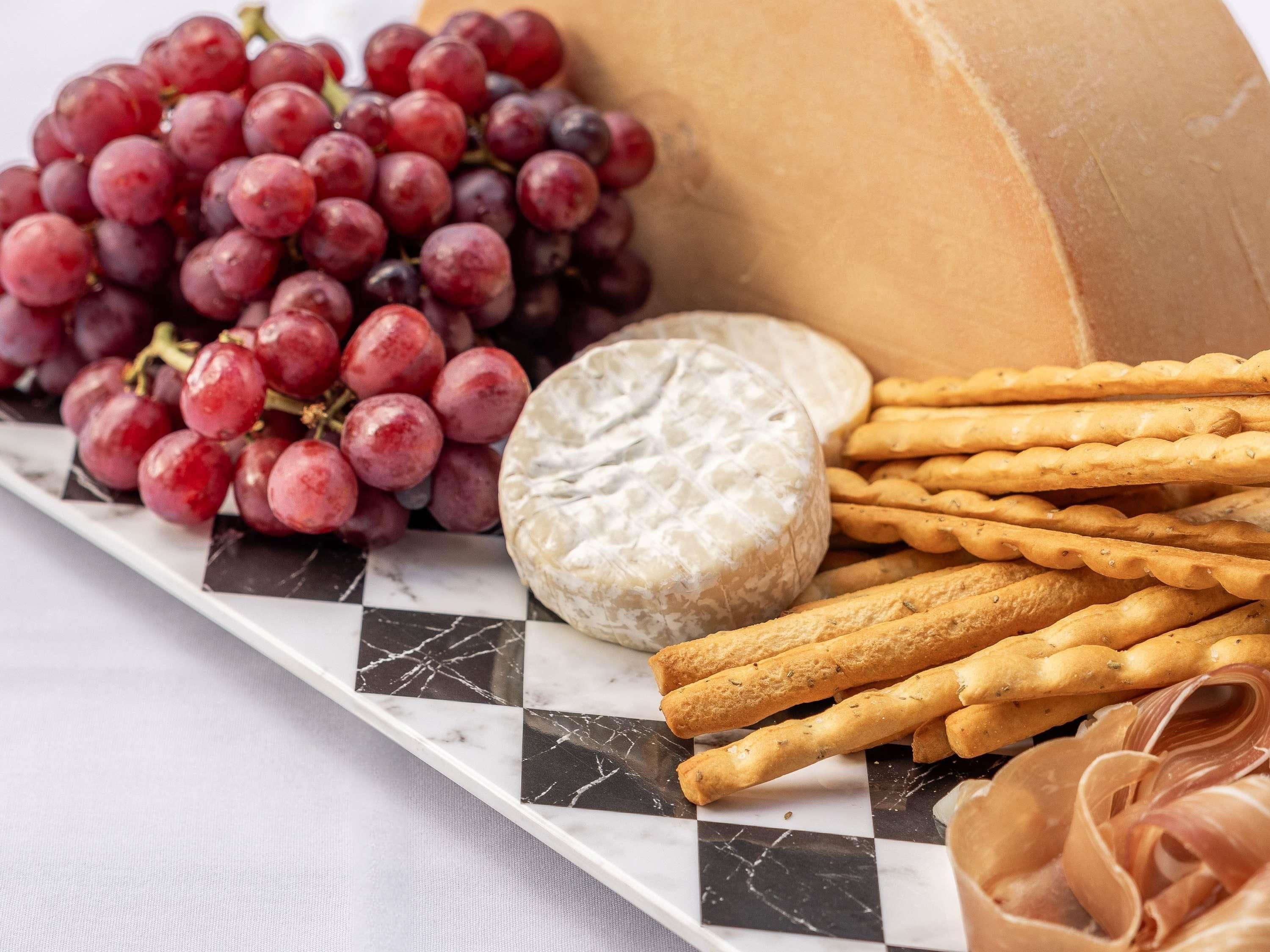 Un plateau de service en marbre, décoré de motifs imitant le marbre, sur lequel on trouve des raisins, un fromage rond, des crackers et des tranches de viande.