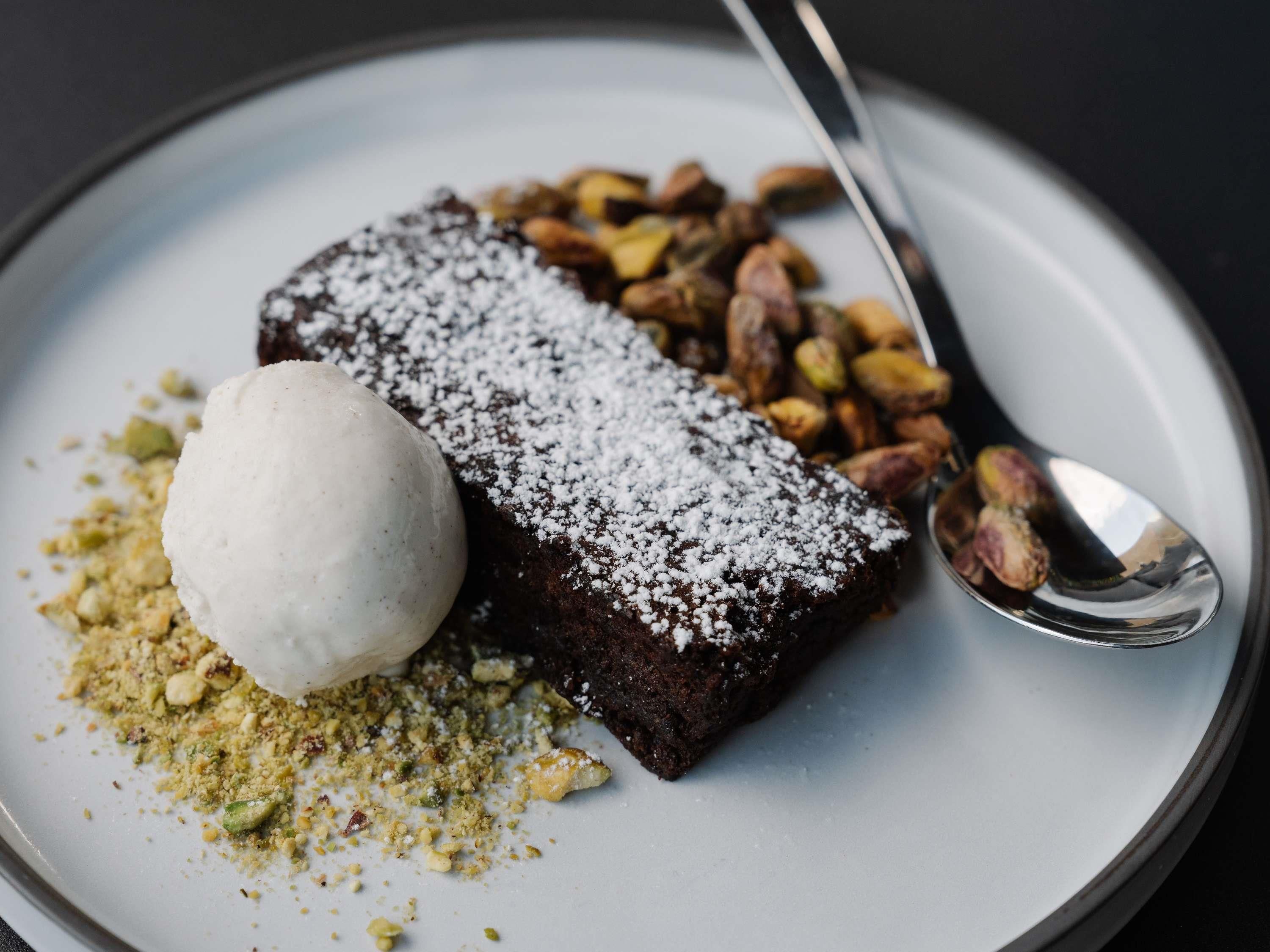 Une assiette de dessert comprenant un brownie, une boule de glace et des noix hachées.