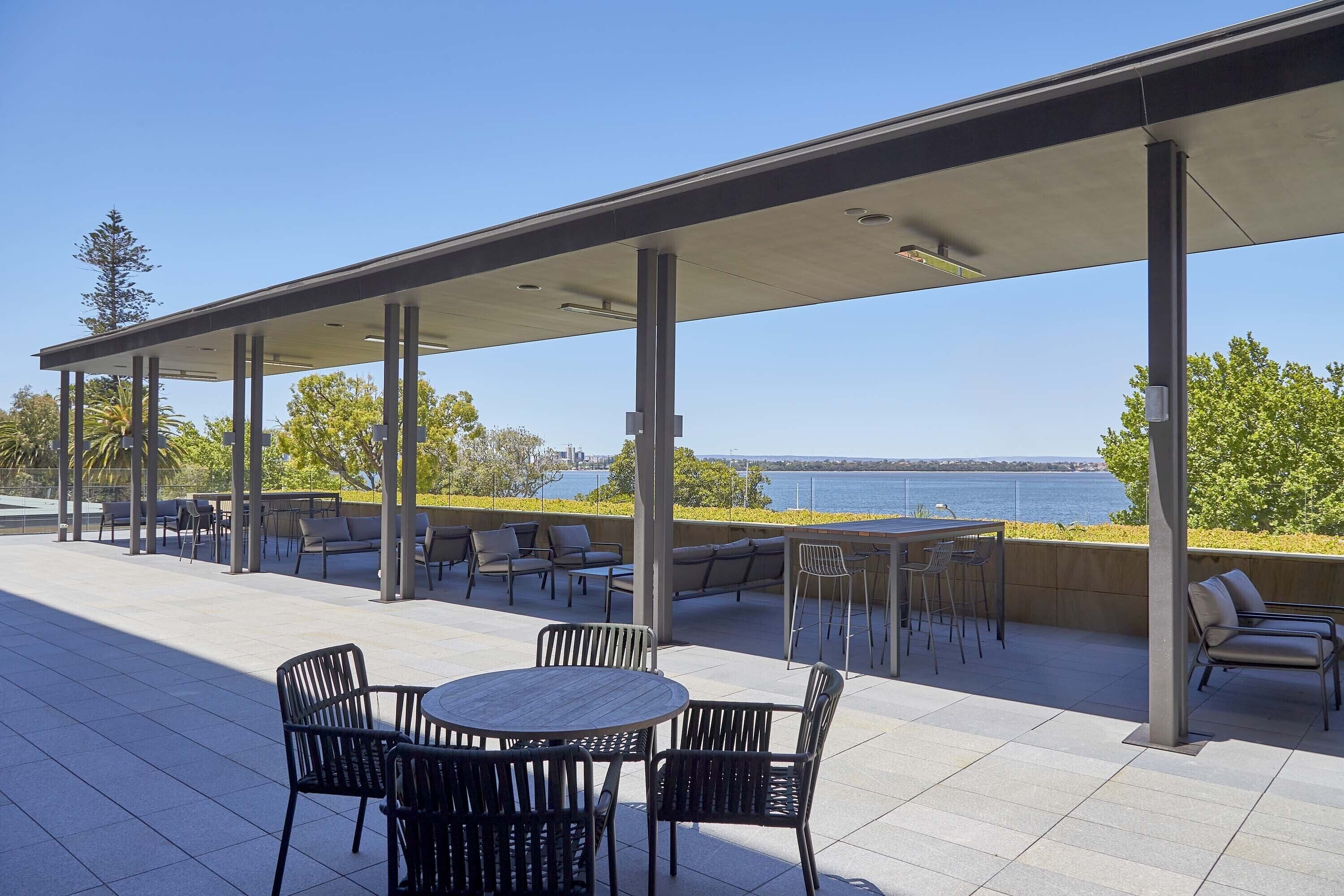 Una terrazza esterna con zona salotto coperta, un tavolo rotondo con sedie e vista sull'acqua.