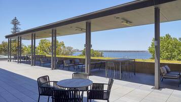 Una terrazza esterna con zona salotto coperta, un tavolo rotondo con sedie e vista sull'acqua.