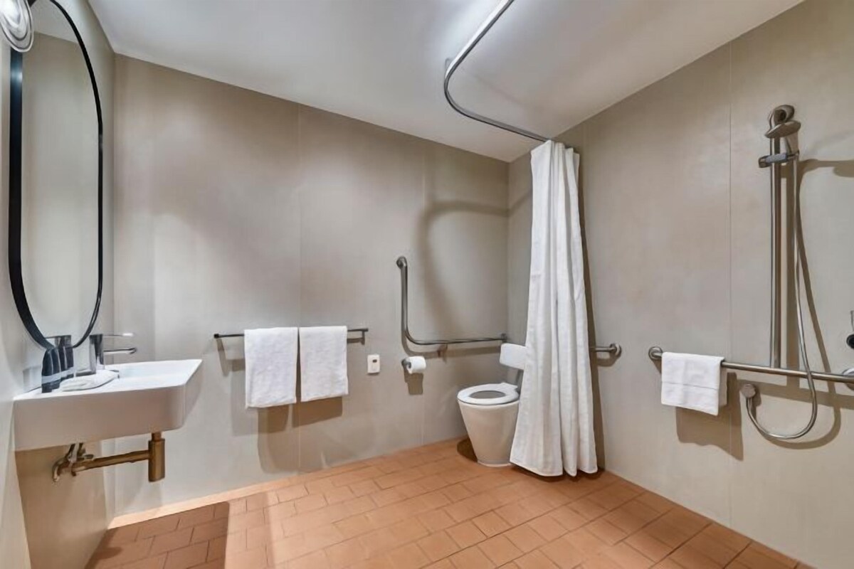Un baño con lavamanos, inodoro, ducha y barras de apoyo.