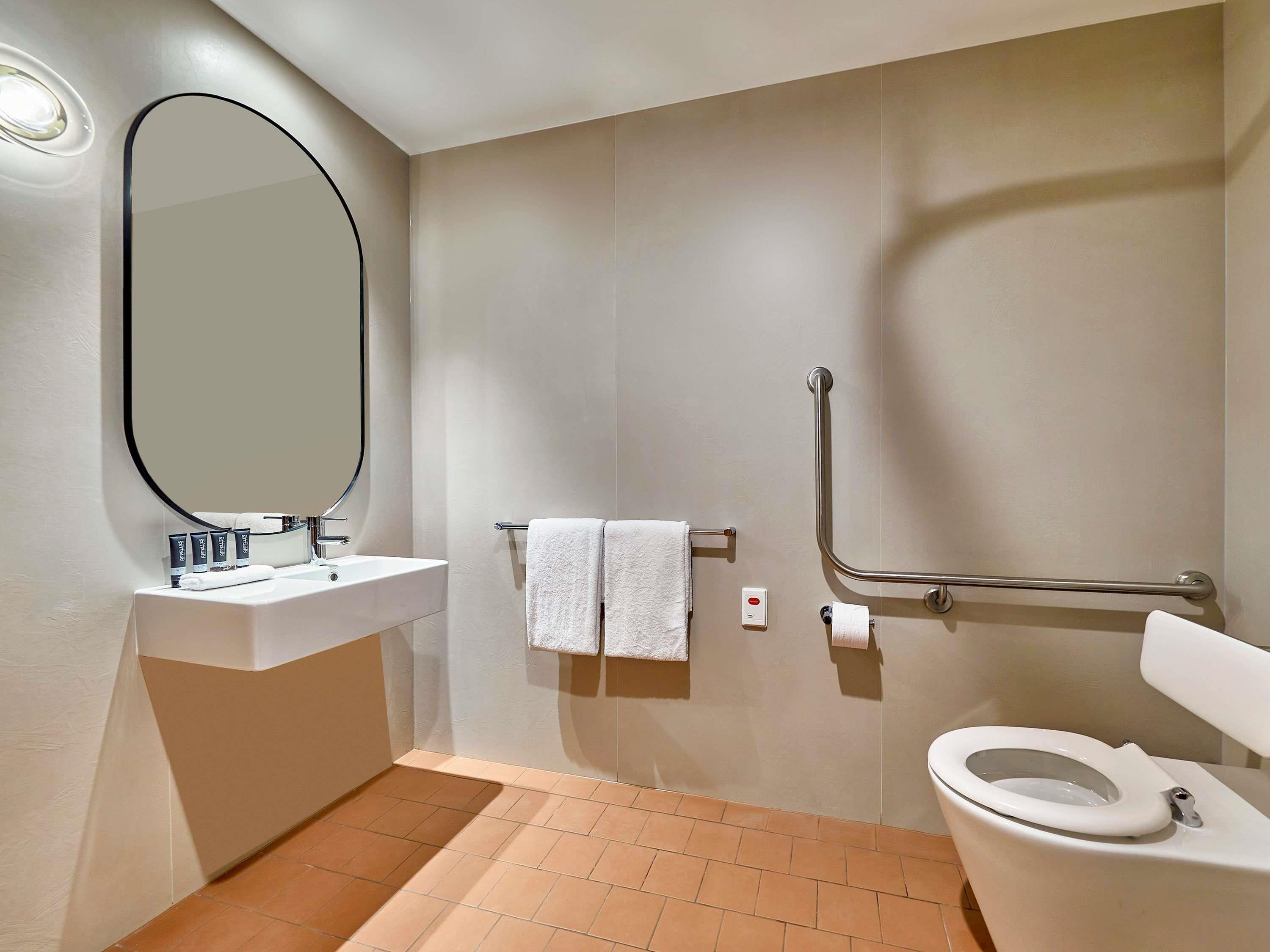 Un baño moderno con lavamanos, espejo, inodoro y barras de apoyo.