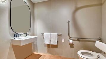 Un baño moderno con lavamanos, espejo, inodoro y barras de apoyo.